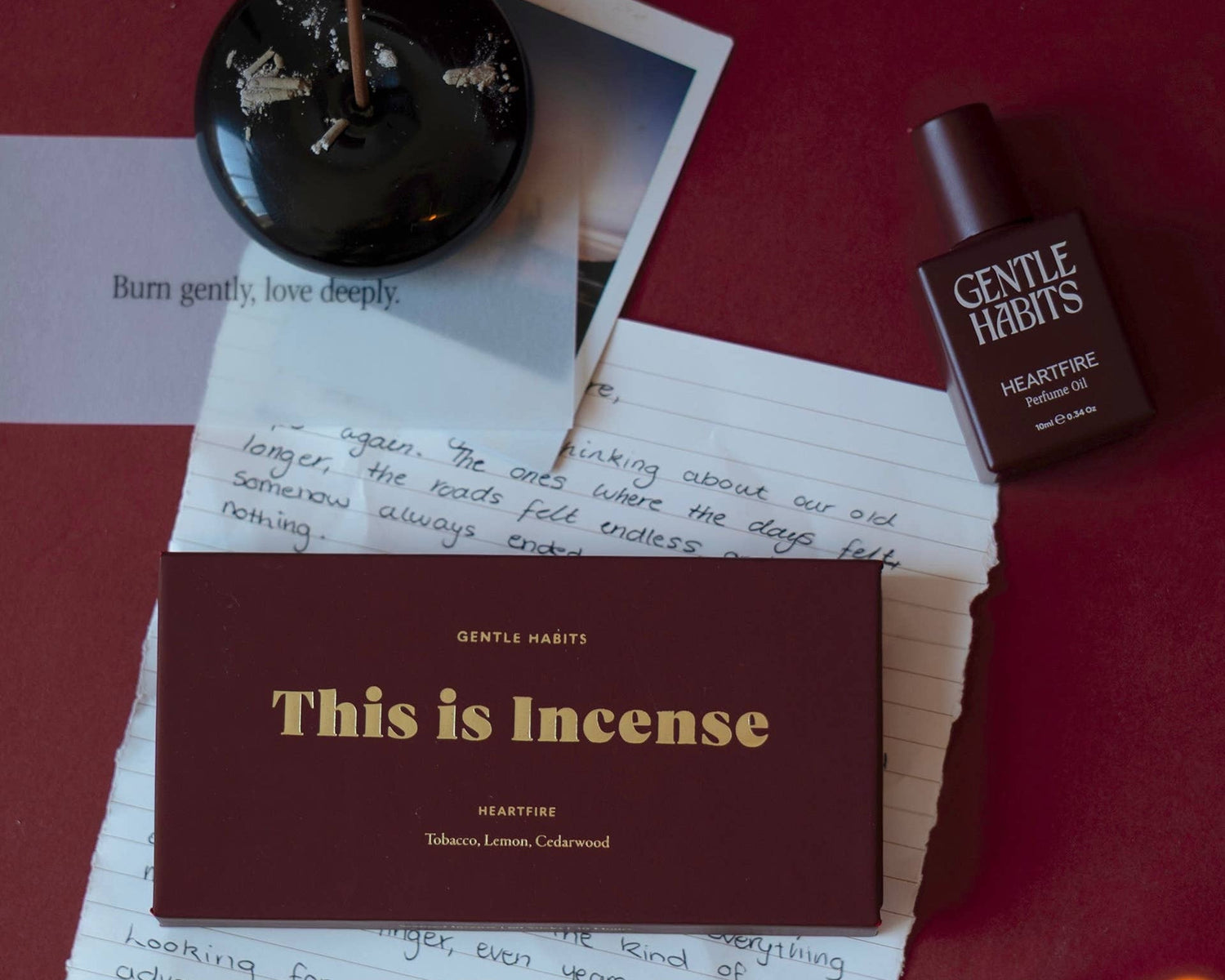 Incense stick, bottle of Gentle Hauts product, and lit candle on a red surface with a card reading 'This is Incense'.